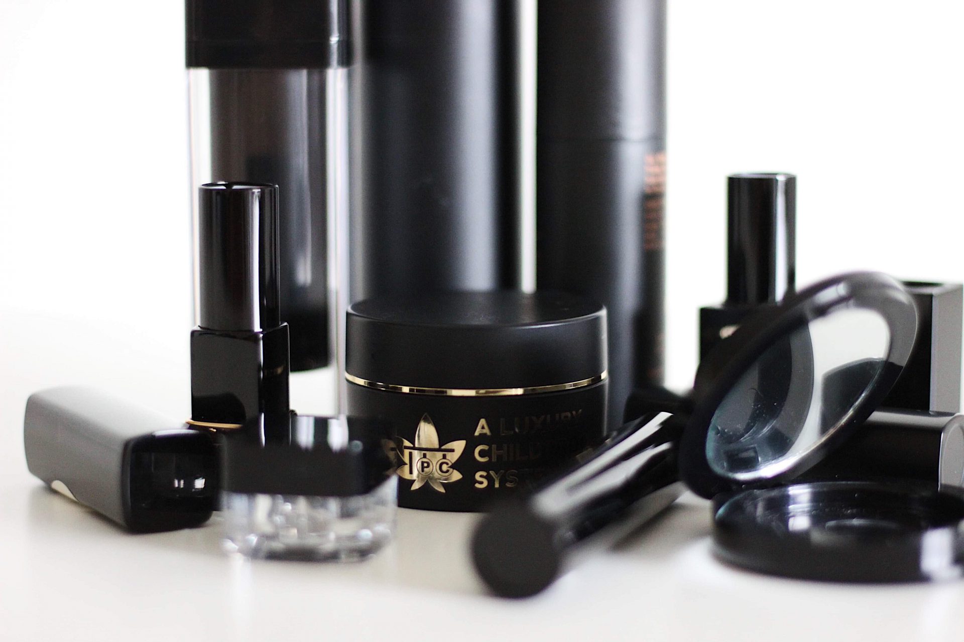 The Packaging Company Family set of matte black airless bottles, cosmetic jars, compacts, and lipstick cases
